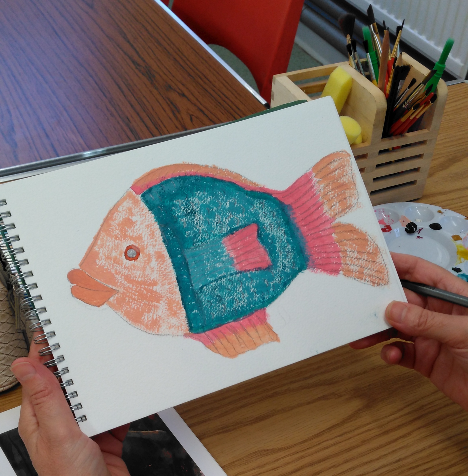 A painting of a fish on a sketchpad held by the artist