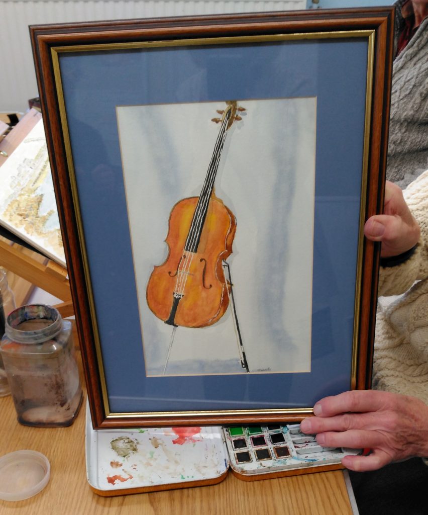 A framed watercolour paining of a cello being held by the artist.