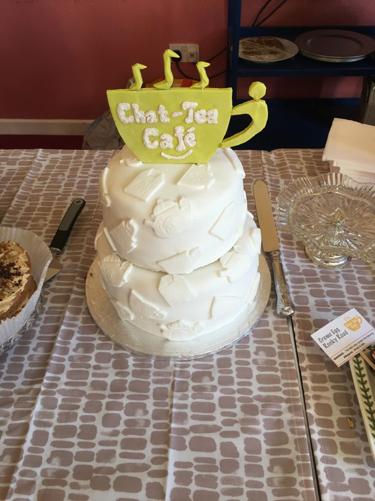 Picture of white iced cake with Chat-Tea Cafe Logo in green icing on top.