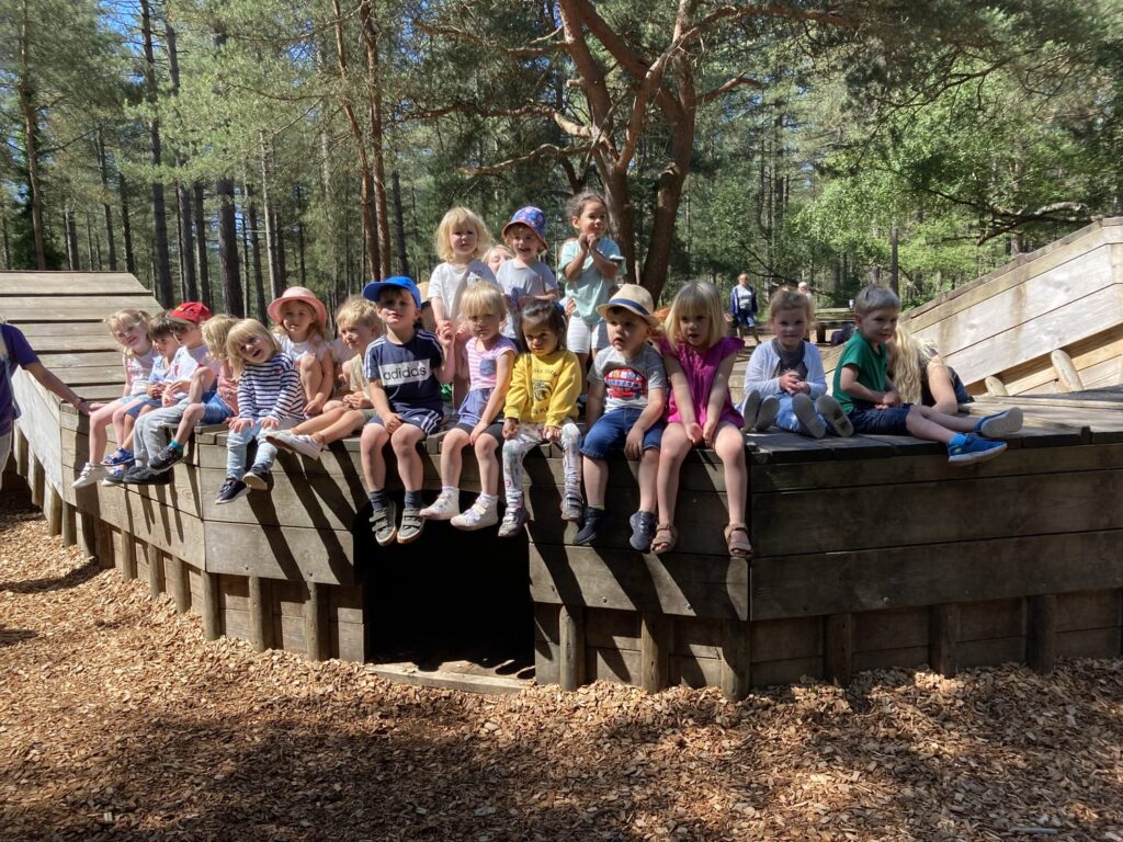 Children from Badger Farm Pre-school sitting on a wooden structure at Moors Valley Country Park