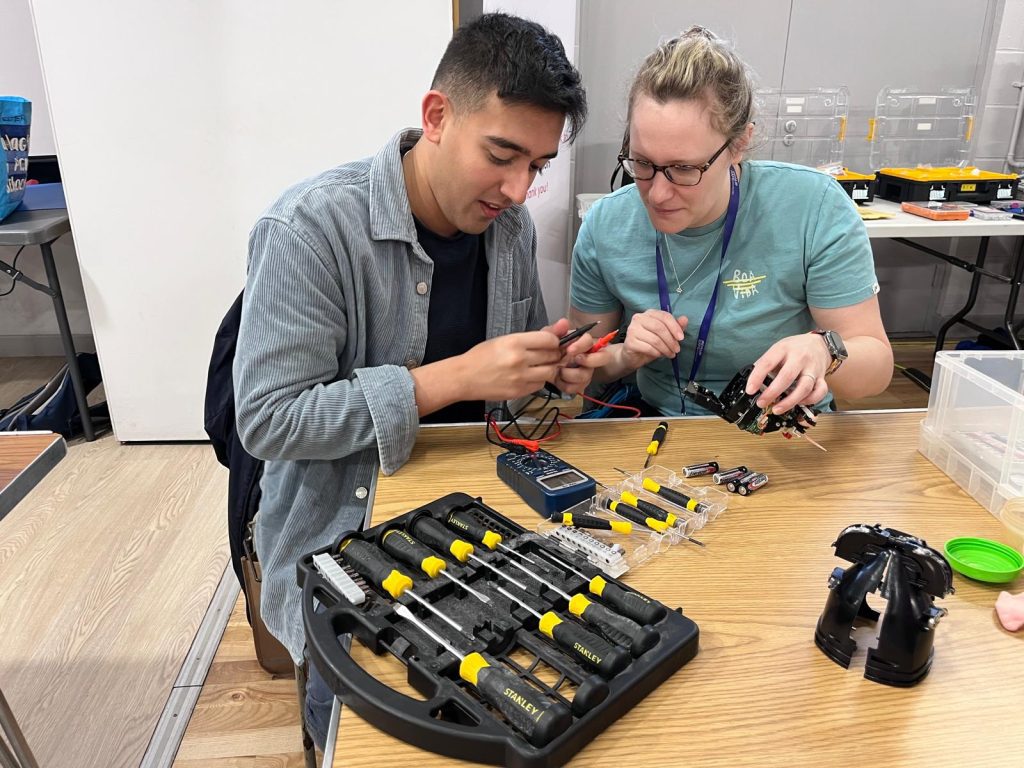 A man and a woman with a set of tools testing a gadget at Repair Café Winchester.