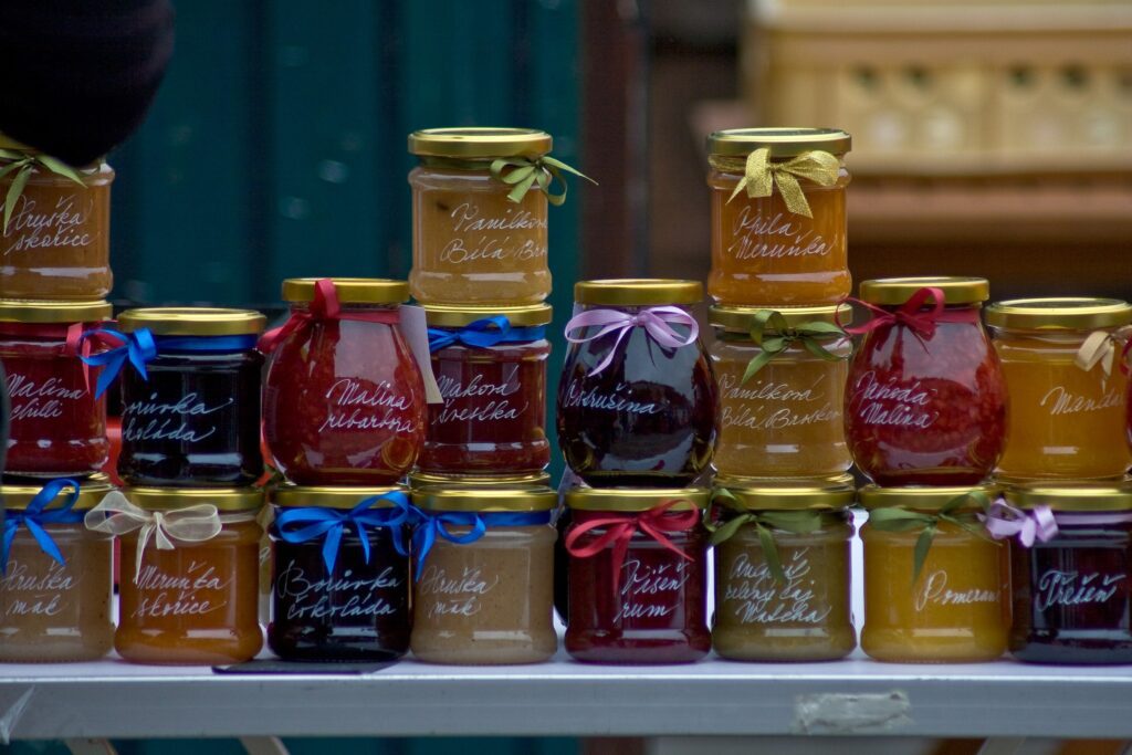 A display of homemade jam jars arranged in rows, each with a gold lid, colourful ribbon, and handwritten fruit‑flavour label.